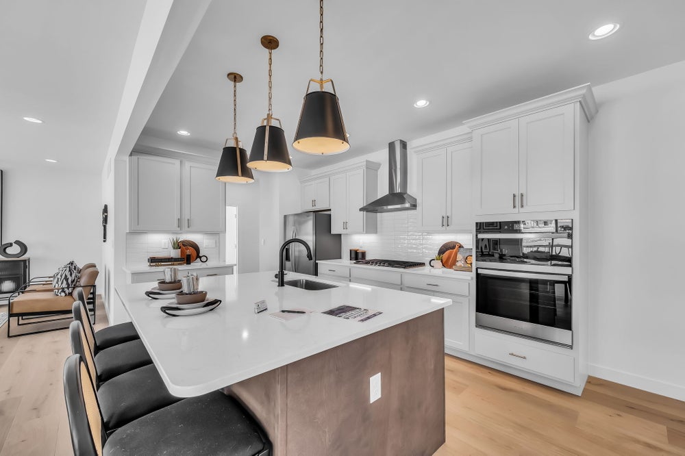 A contemporary kitchen featuring white cabinetry, a wood-tone island with seating, bold black pendant lighting, stainless steel appliances, and a sleek, open layout.